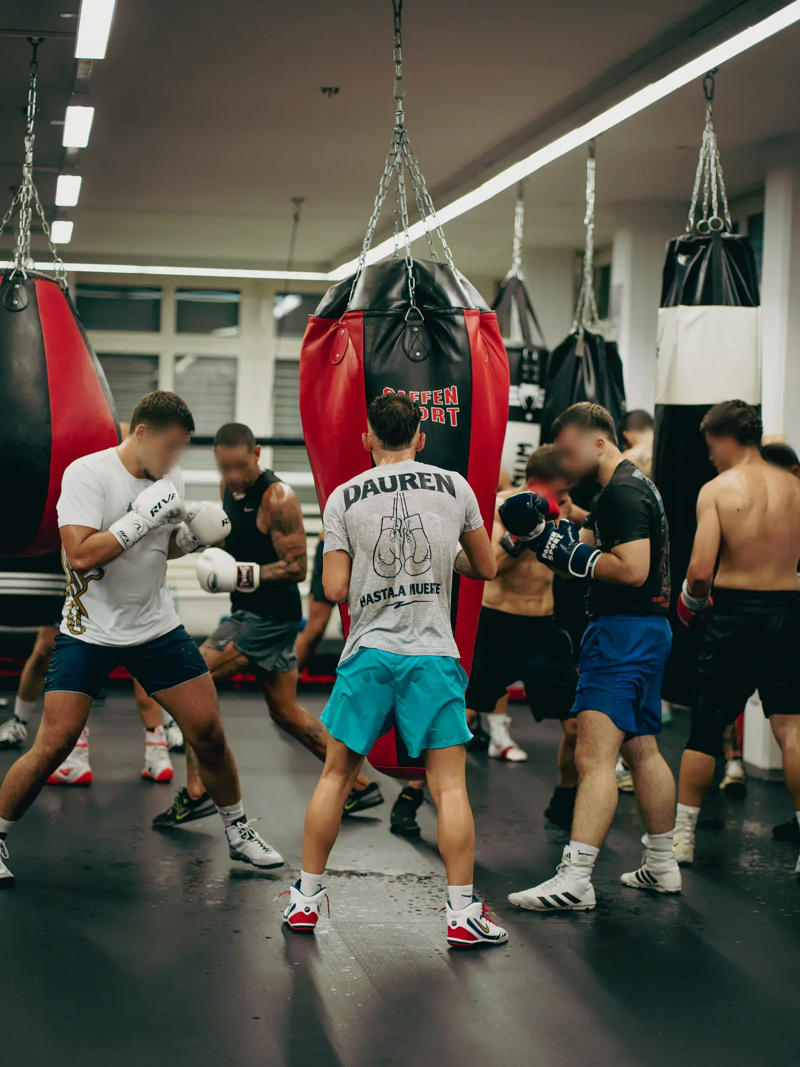 Several gloved boxers drill in pairs between red and black heavy bags.