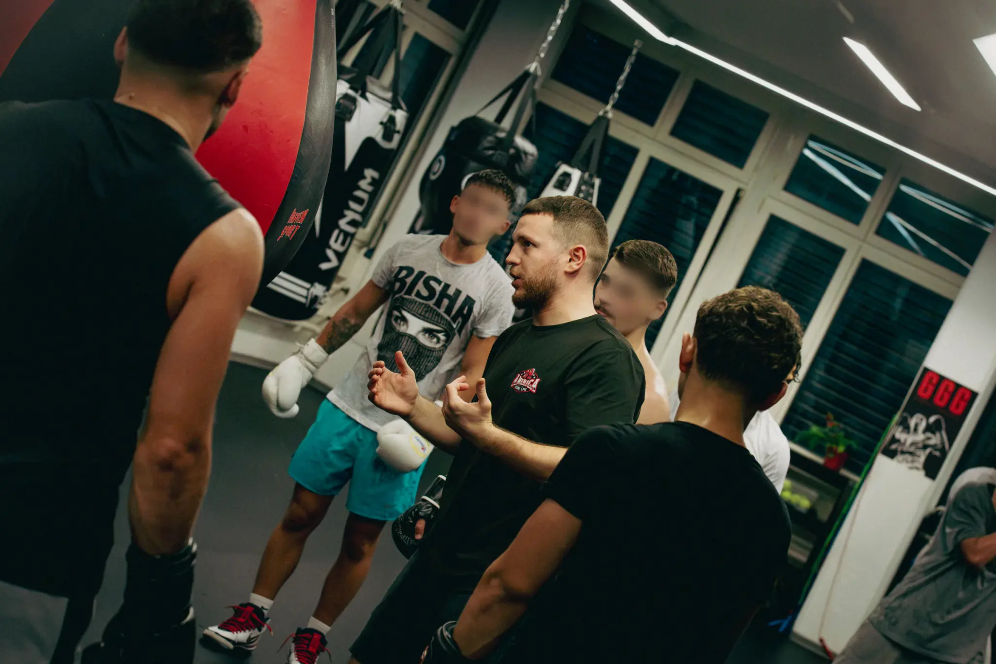 Coach in a black America Boxing shirt explains the next drill to a group of gloved boxers.