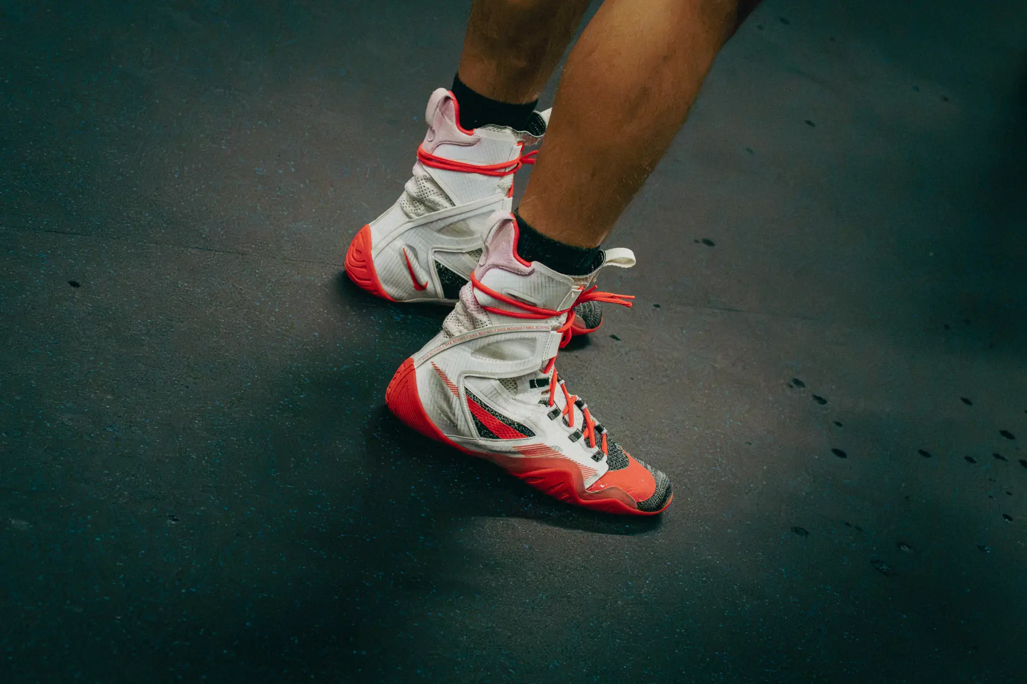 Red and white boxing shoes in motion on the dark training mat.