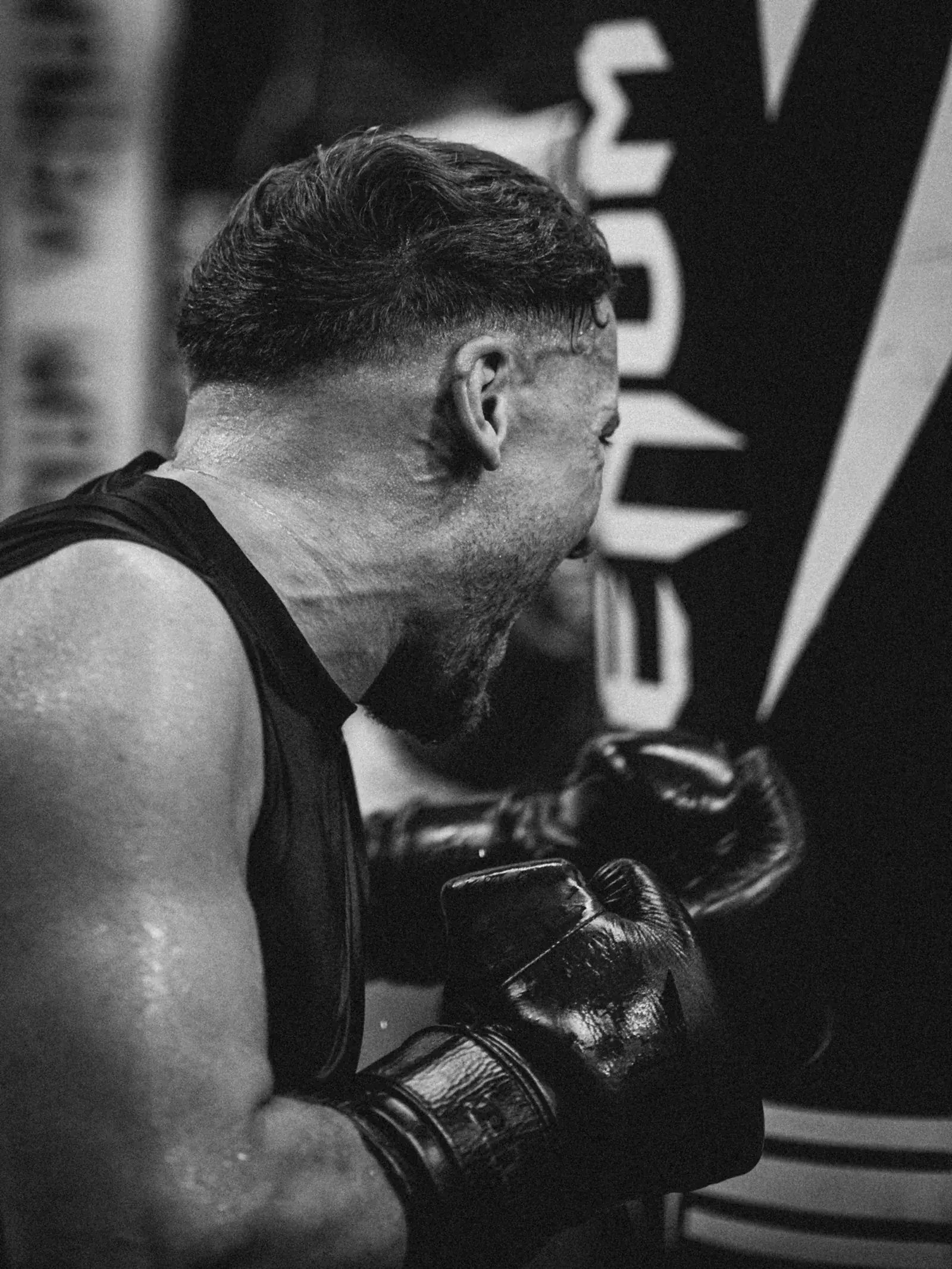 Black-and-white photo of a sweating boxer hitting a heavy bag at full power.