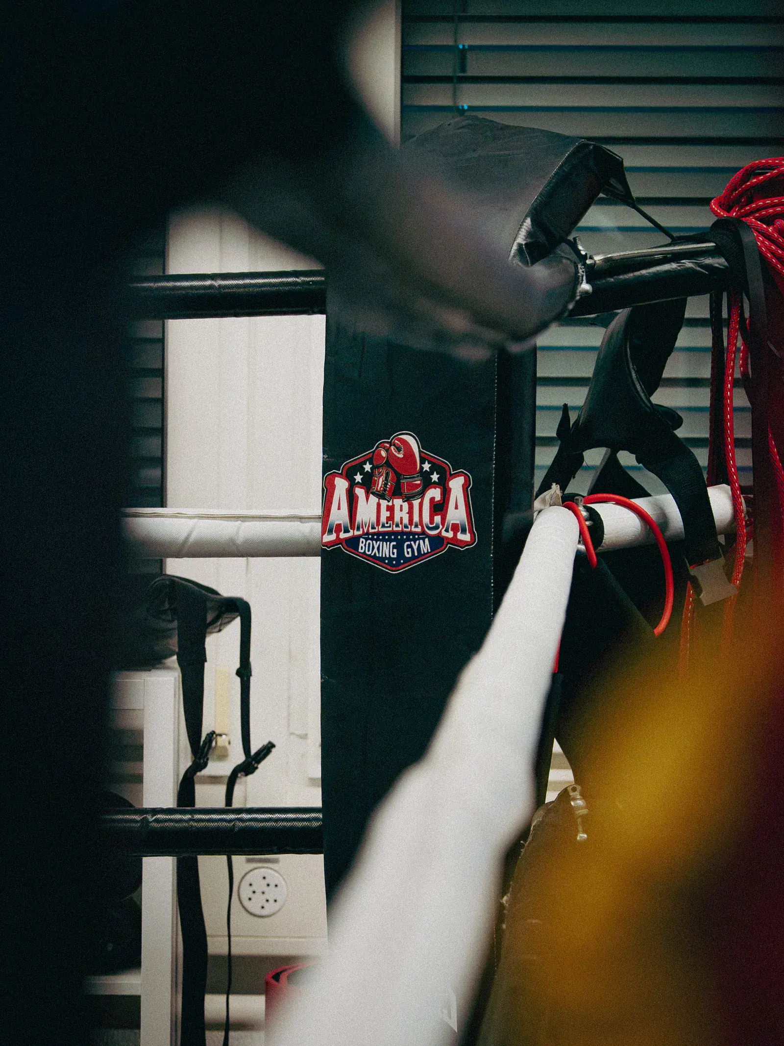 Ring corner with the America Boxing Gym logo on the corner pad and the white ring ropes in front.